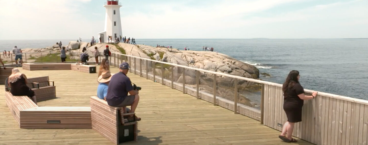 People sitting on benches and looking at ocean and lighthouse on rocks in distance